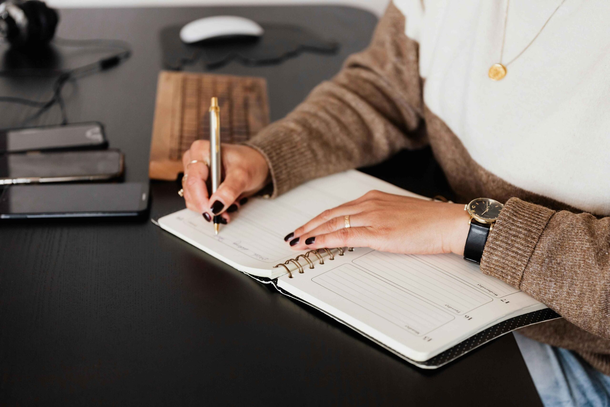 A woman writing on a planner on a black desk.